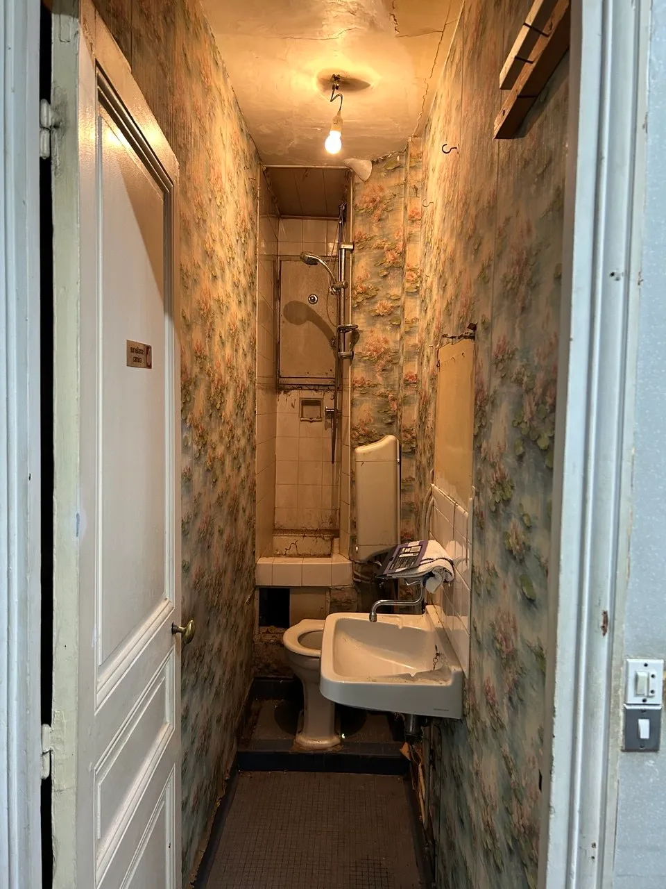 L'ancienne salle d'eau avant travaux, étroite et tapissée d'un papier peint fleuri